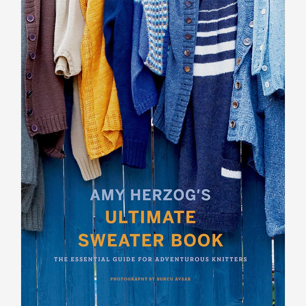 The cover of a book titled "Amy Herzog's Ultimate Sweater Book: The Essential Guide for Adventurous Knitters." The image shows various knitted sweaters in different colors hanging on hooks against a blue wooden background. Photography by Burcu Avsar.
