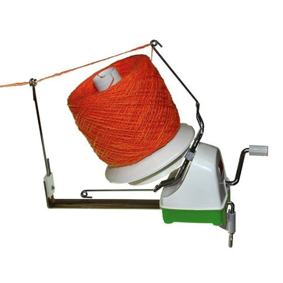 A yarn winder with an orange spool of yarn. The device includes a metal arm and a manual crank handle for winding the yarn. The setup appears to be in working position, with the yarn threaded through the guide arm and ready to be wound.