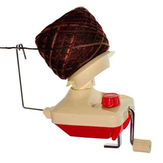 An automatic yarn ball winder with a red and white plastic body, a metal winding arm, a small crank handle, and a large skein of brown yarn in place. The yarn threads through a metal guide wire and the red dial appears to control the winding speed.