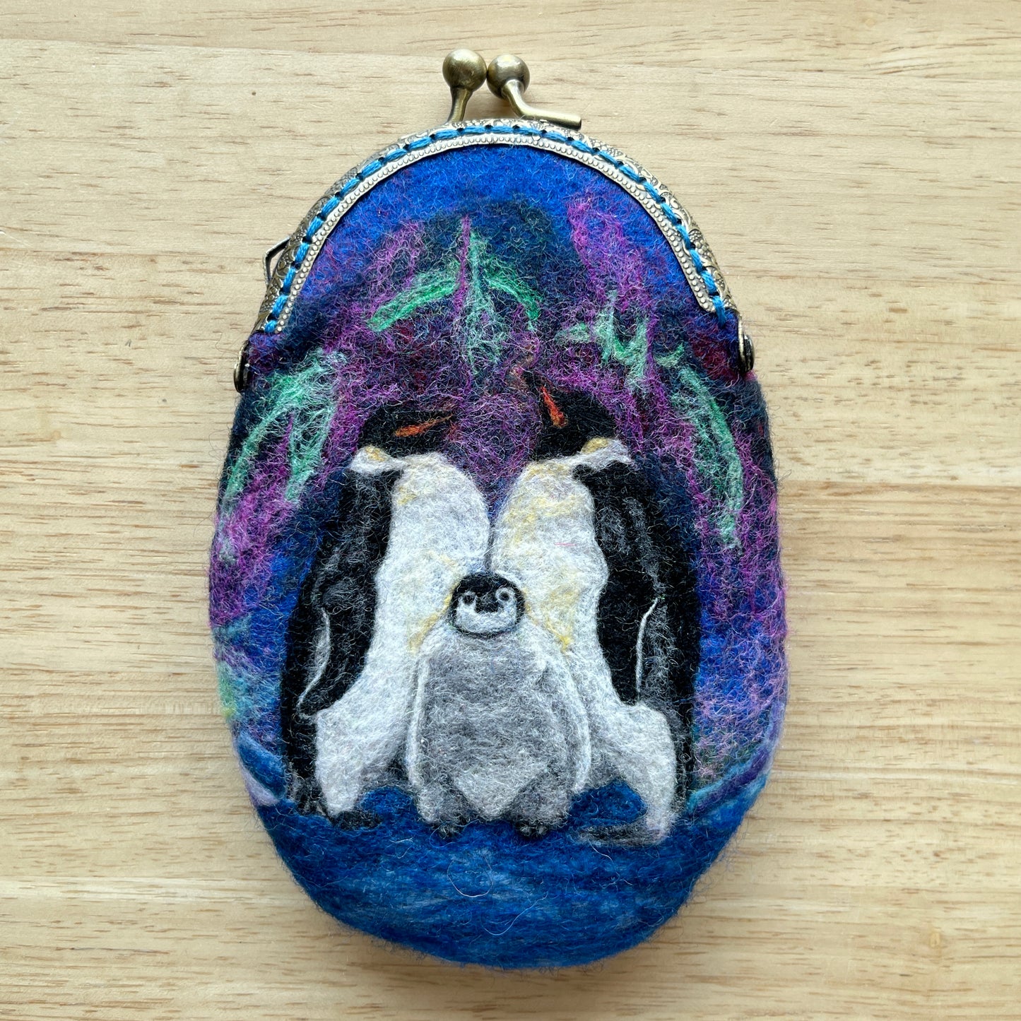 Oval-shaped wet felted coin purse with penguin design on a wooden surface
