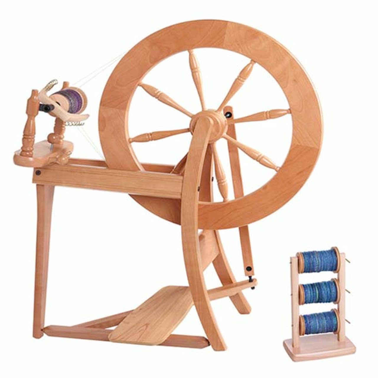 A wooden spinning wheel with a large wheel and a foot pedal. The spinning wheel is accompanied by a stand holding two spools of blue thread. The arrangement is set against a plain white background.