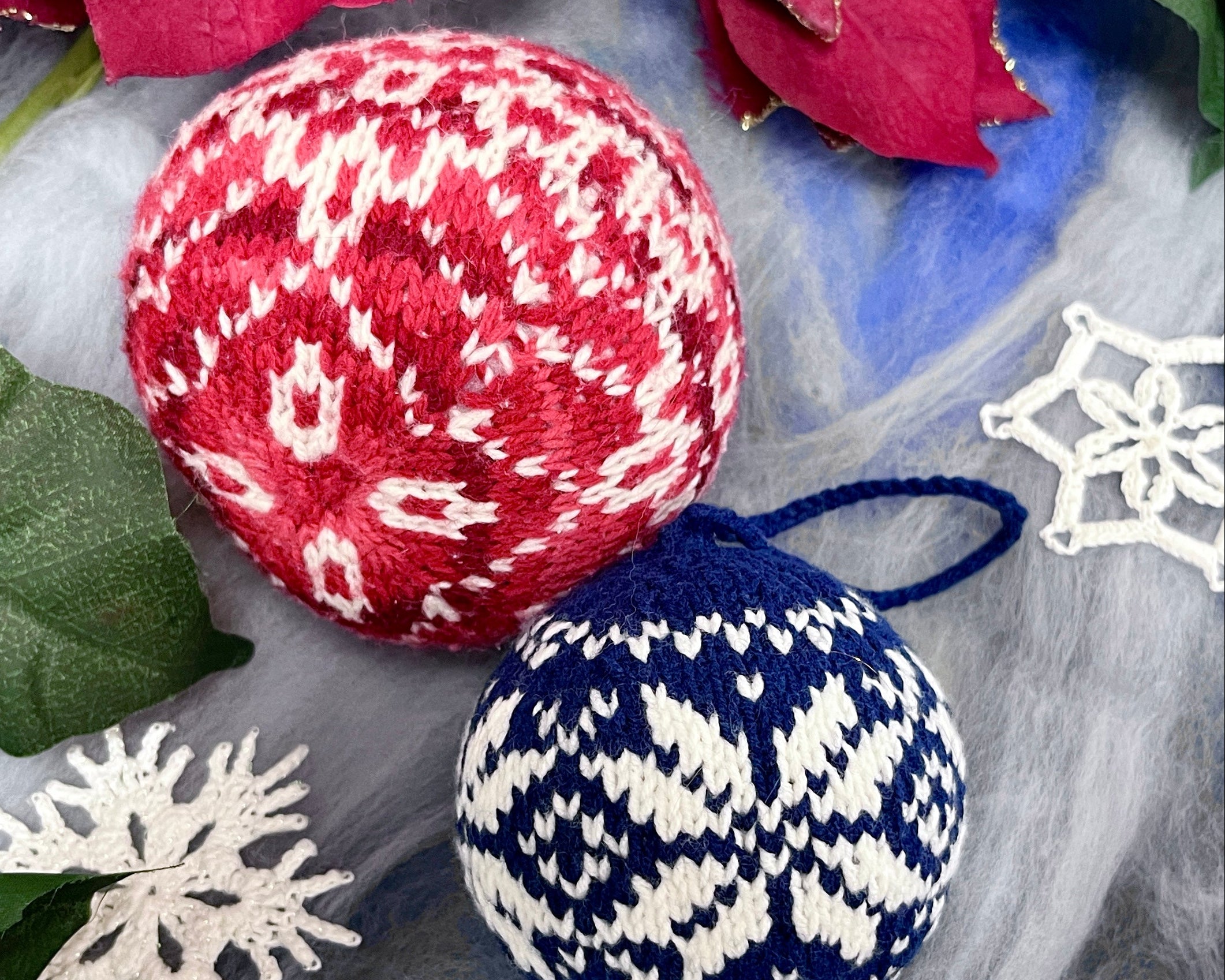 Two knitted Christmas ornaments, one red and white patterned, the other blue and white patterned, on a decorative background with flowers and snowflakes.