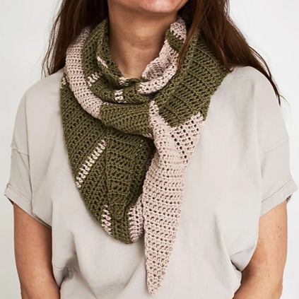 A person is wearing a handmade crocheted scarf with an alternating pattern of olive green and light pink. They are dressed in a light beige T-shirt. The scarf is draped loosely around their neck and shoulders.