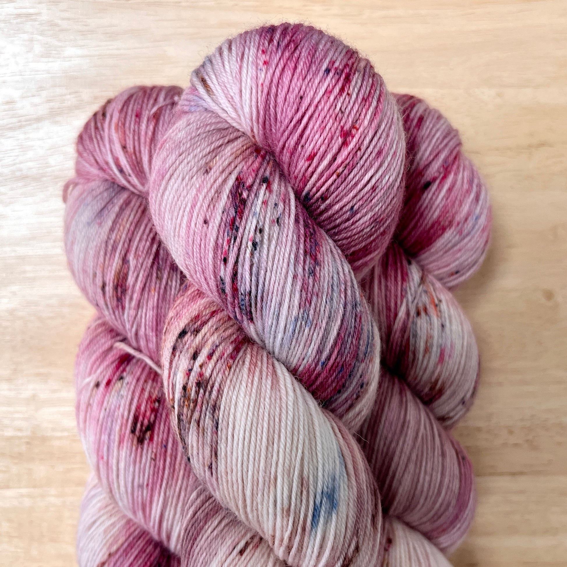 Dusty pink and off white hand-dyed yarn speckled with dark browns and deep indigos.