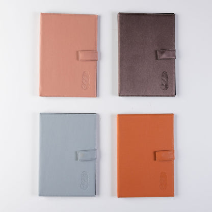 A set of four leather notebooks, one is pink, one dark brown, one light grey, and one orange.