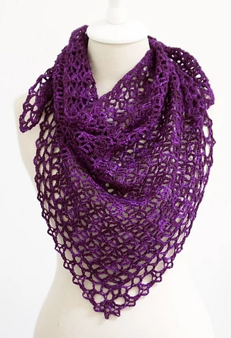 A mannequin displays a vibrant purple, triangular shawl with a detailed open lace pattern. The shawl is draped around the neck and shoulders, showcasing its intricate crochet design.