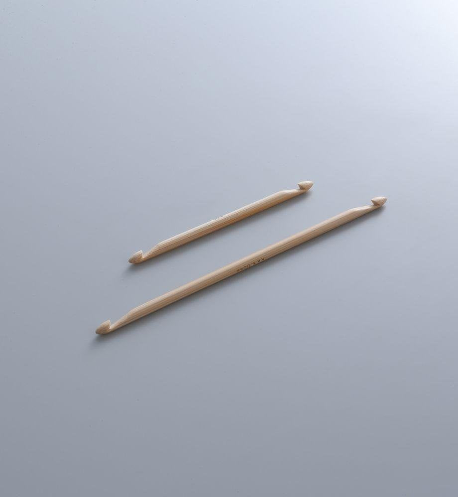 Two double-ended bamboo knitting needles lie on a gray surface. The needles are parallel to each other, with one slightly longer than the other.