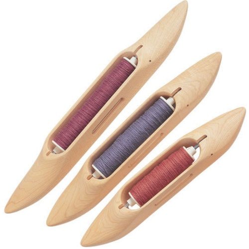 Three wooden weaving shuttles are shown, each containing a spool of thread in different colors: pink, purple, and red. The shuttles are smooth and elongated, designed for use in a loom.