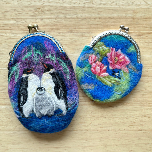 Two felted coin purses with penguin design and floral design on a wooden surface