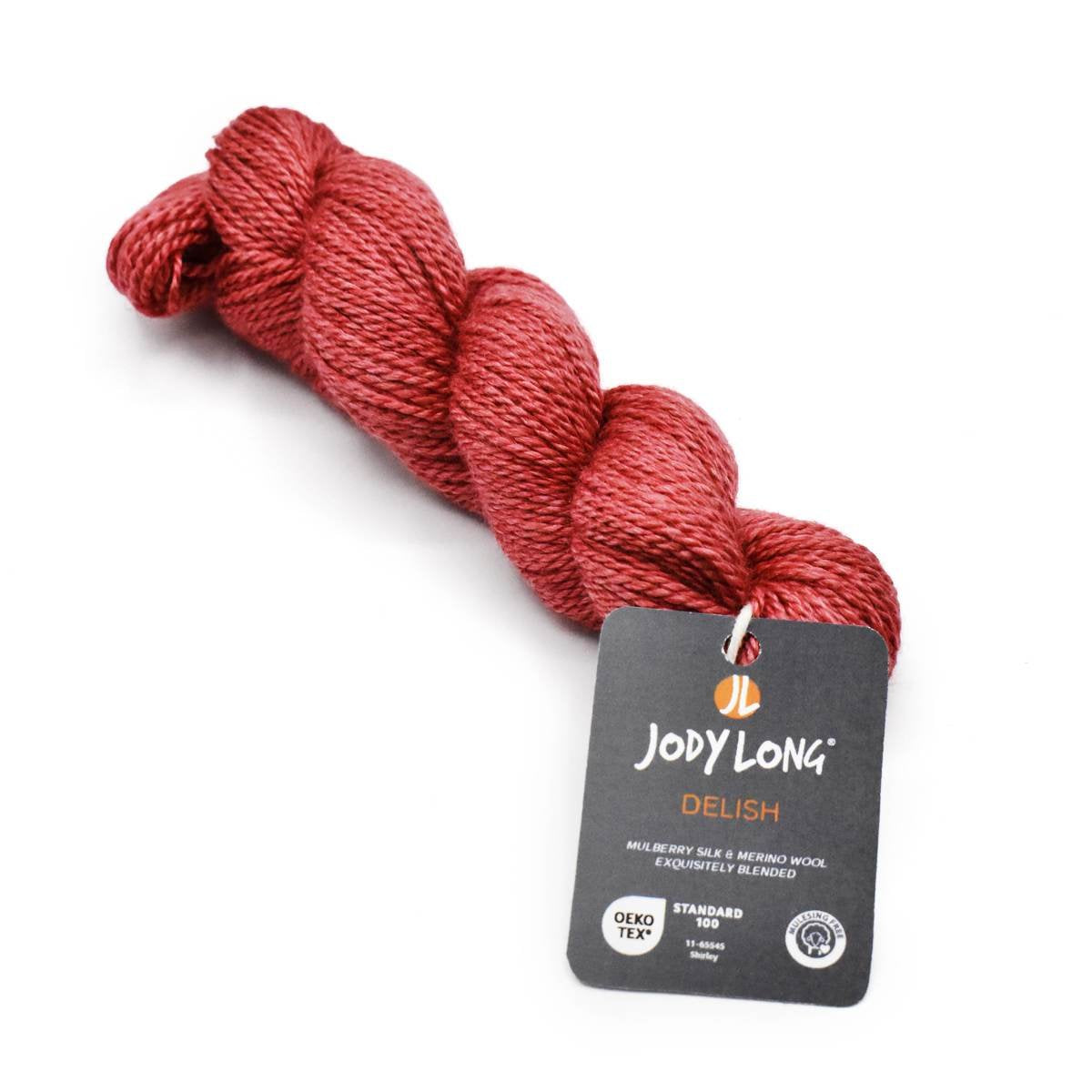 A twisted skein of red yarn is shown with a tag reading "Jody Long Delish." The label indicates that the yarn is a blend of mulberry silk and merino wool, meeting OEKO-TEX standards.